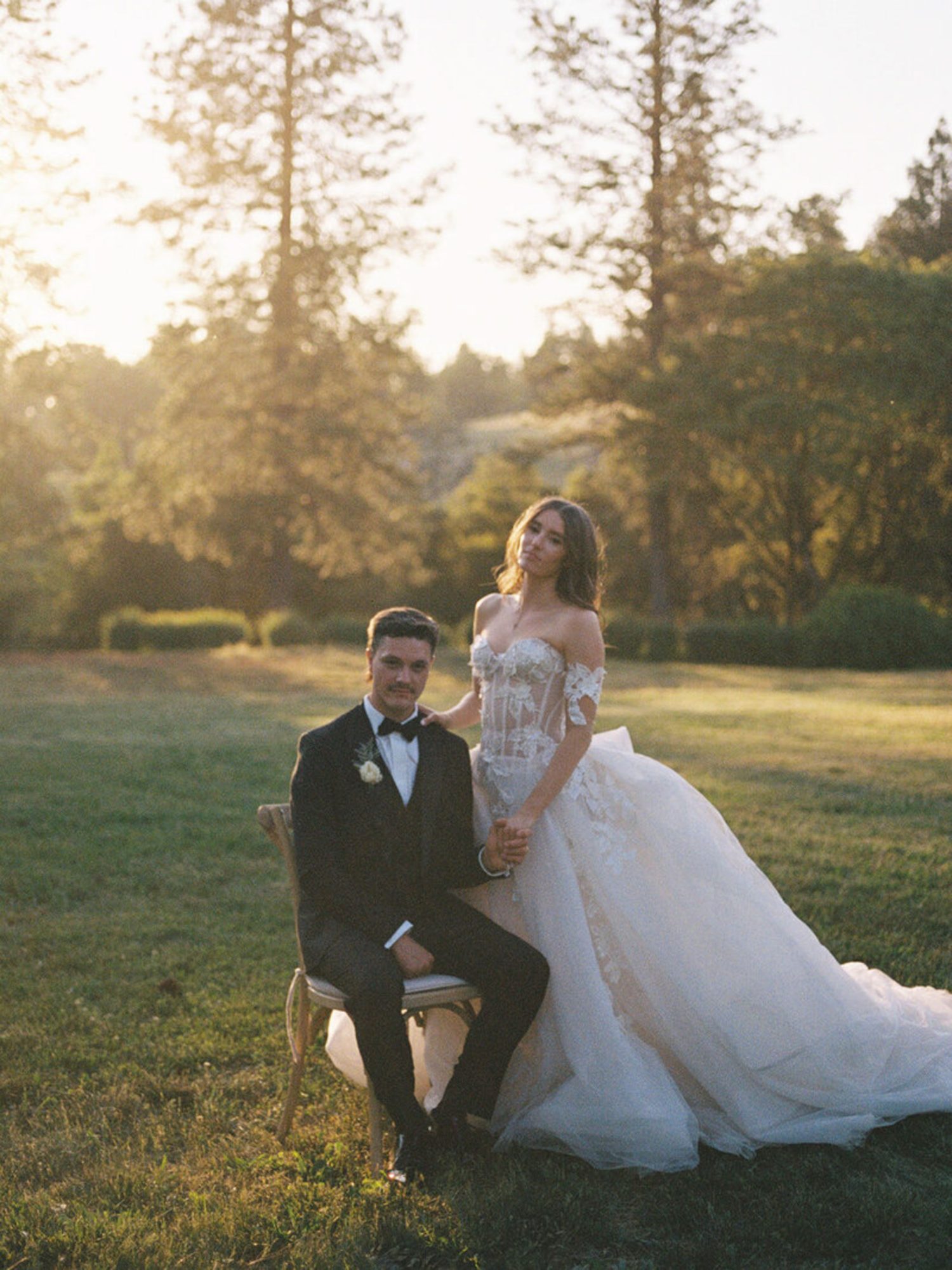 Bride and groom on a lawn at sunset surrounded by trees